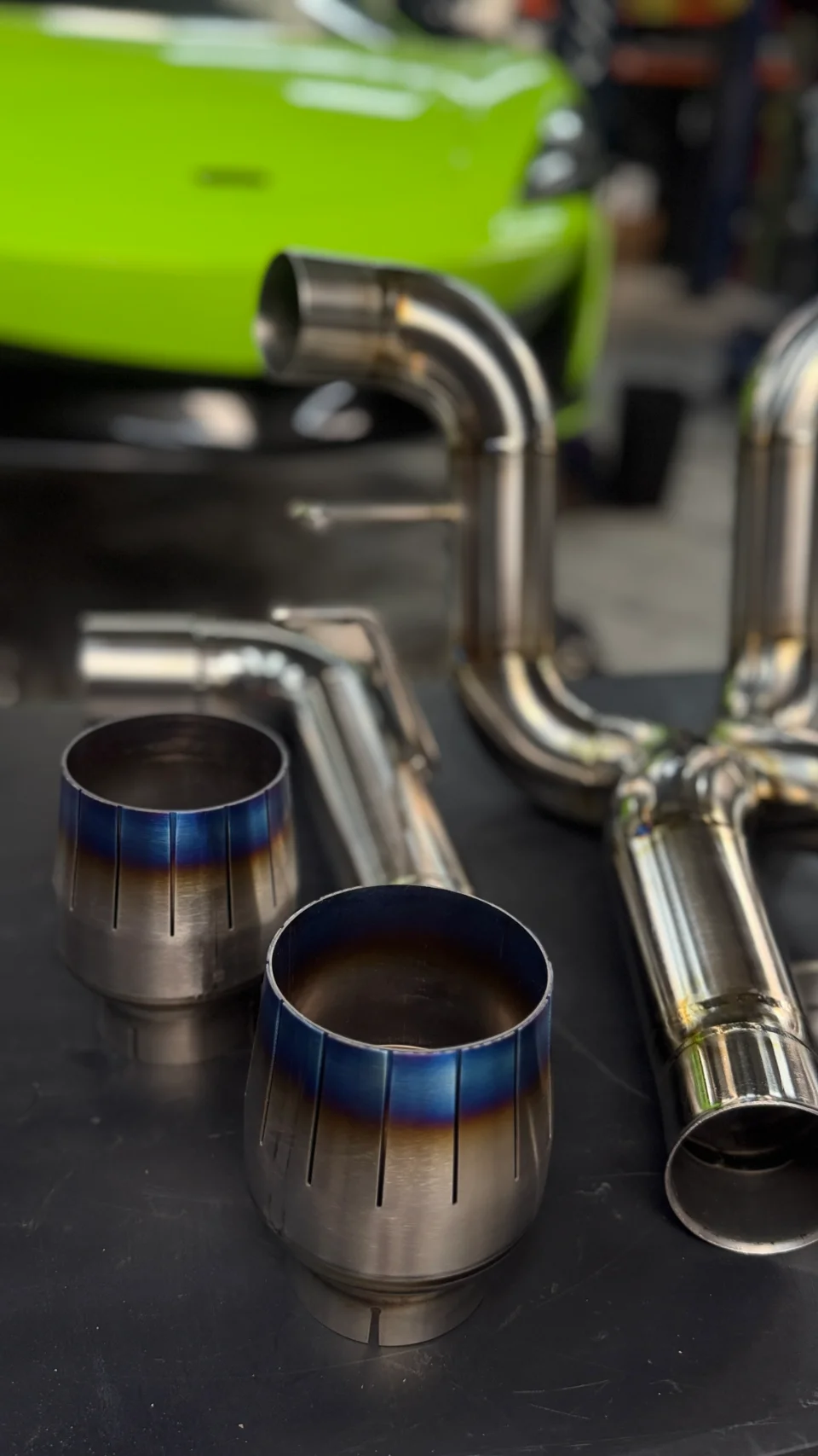 Custom fabricated titanium exhaust components with heat-treated tips for a high-performance car in a shop setting.