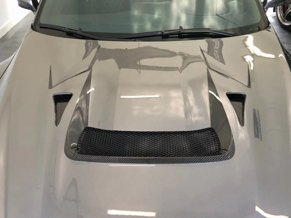 A close-up view of a grey car's carbon fiber hood featuring a large central scoop and aggressive side vents.