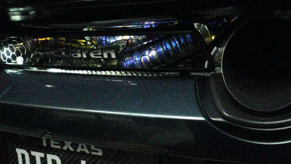 Close-up of a McLaren's rear bumper and exhaust system, featuring heat-treated titanium tips and the McLaren logo.