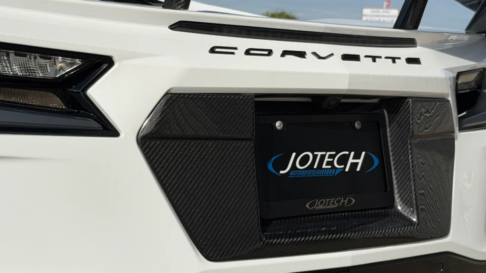 Rear detail of a white C8 Corvette featuring carbon fiber trim, taillight, and a Jotech Motorsports license plate frame.