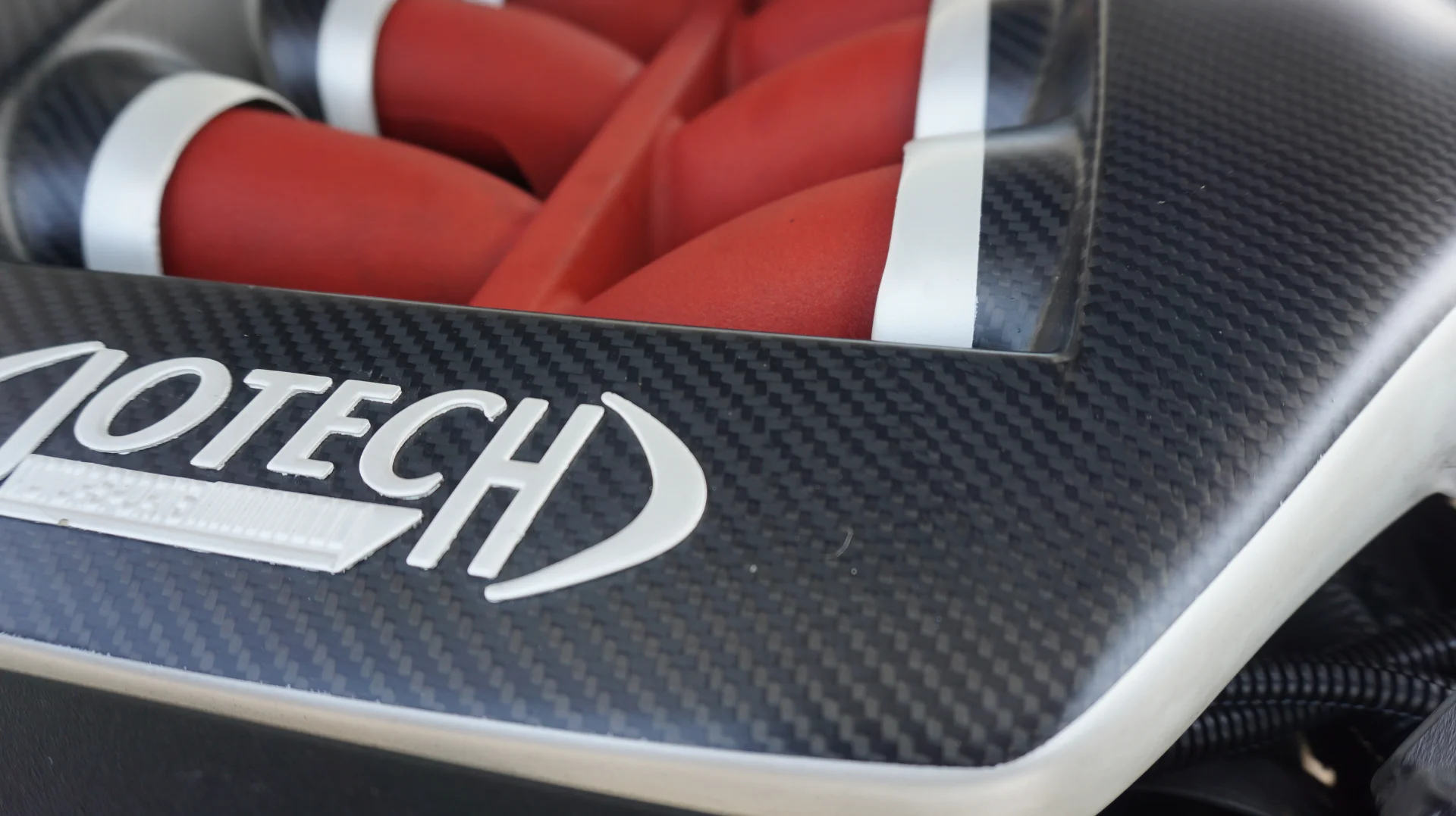 Close-up of a Jotech carbon fiber intake manifold with red runners in an engine bay.