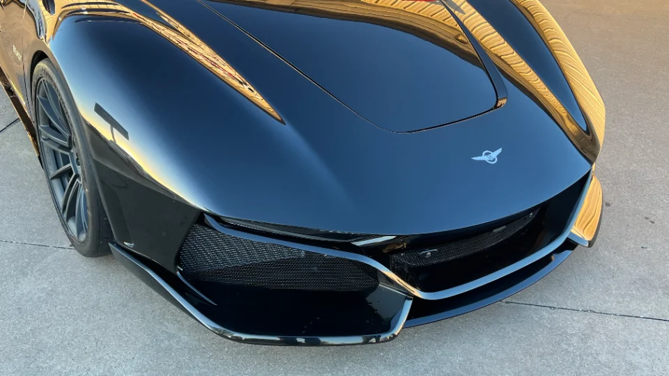 A sleek black exotic car with a highly reflective finish, showcasing its front bumper, grille, and hood design.