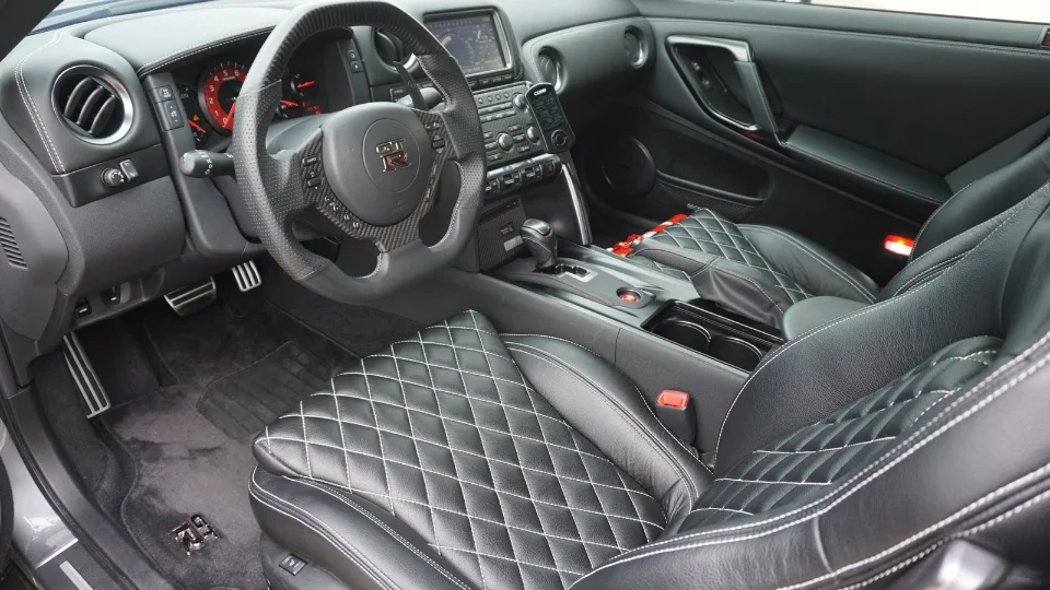Detailed view of a Nissan GT-R interior featuring custom black leather seats with white diamond stitching and a carbon fiber steering wheel.