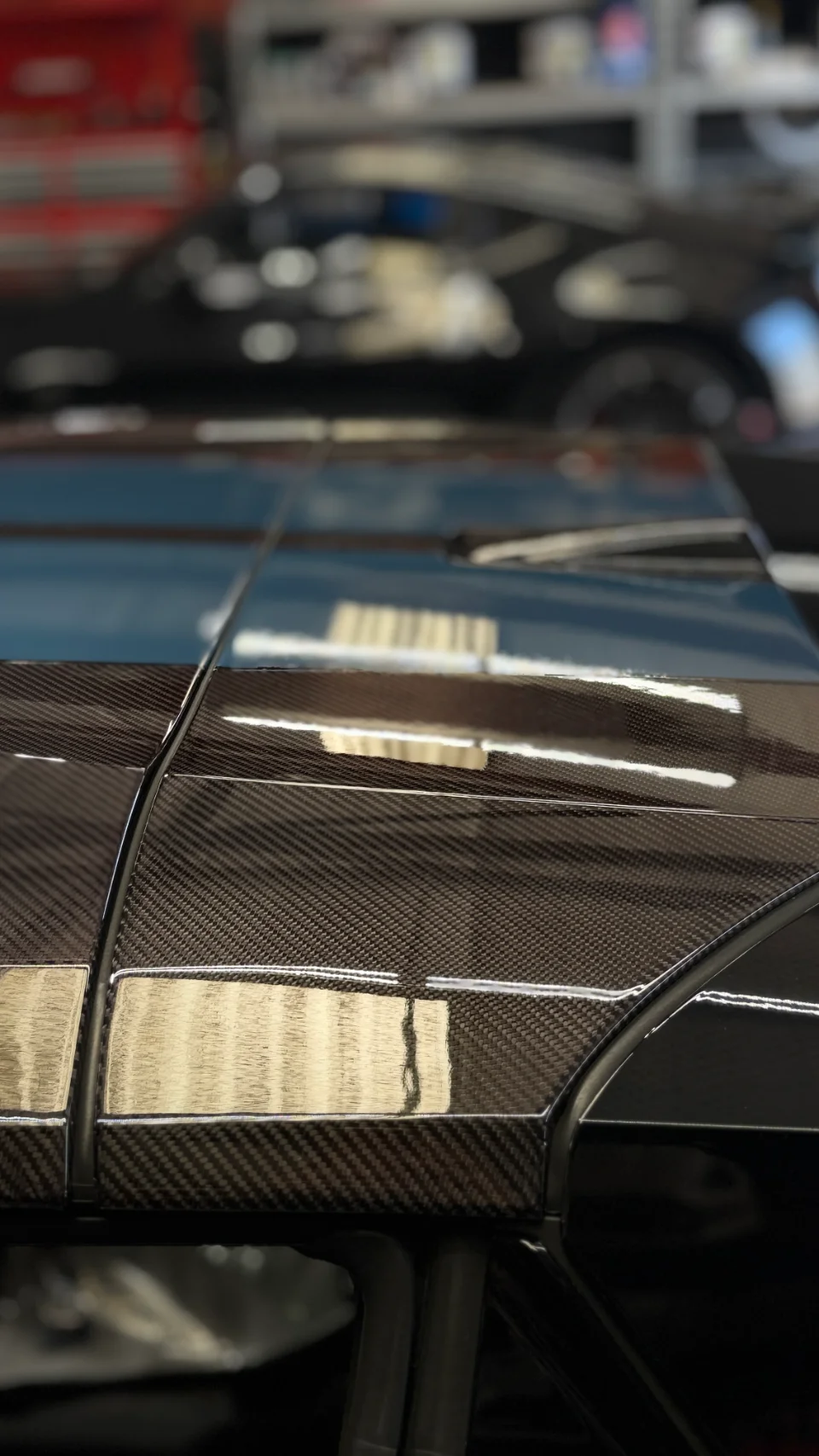 Close-up detail of a glossy carbon fiber rear deck or trunk lid on a performance car in a shop environment.