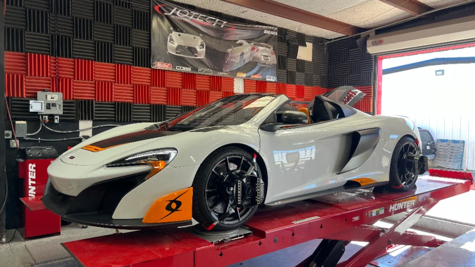 A white McLaren supercar on a red Hunter dyno at Jotech Motorsports performance tuning shop.