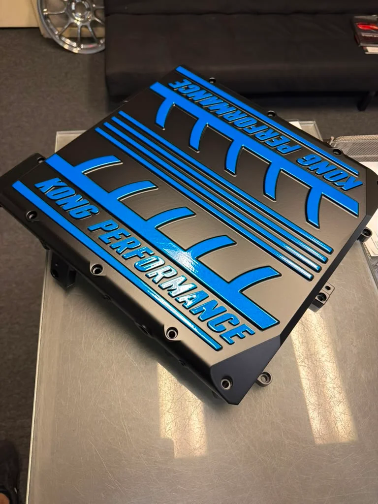 A black and blue Kong Performance supercharger lid on a metal table, showcasing the detailed design.