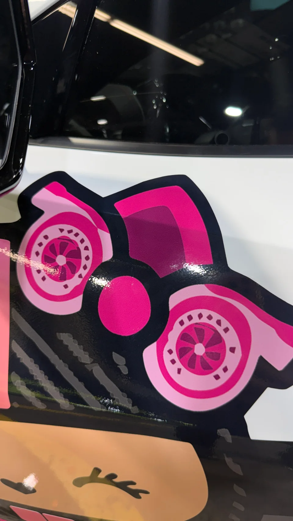 Close-up of a pink twin turbocharger graphic decal on the side of a white performance car.
