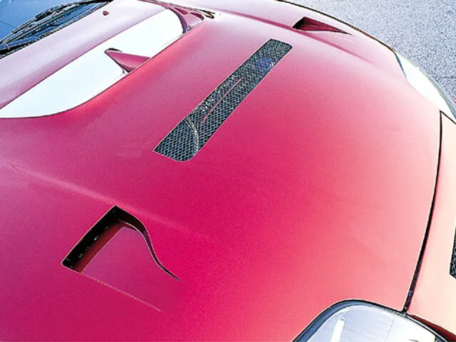 Close-up of a red car's custom hood with performance vents, showcasing exterior modifications.