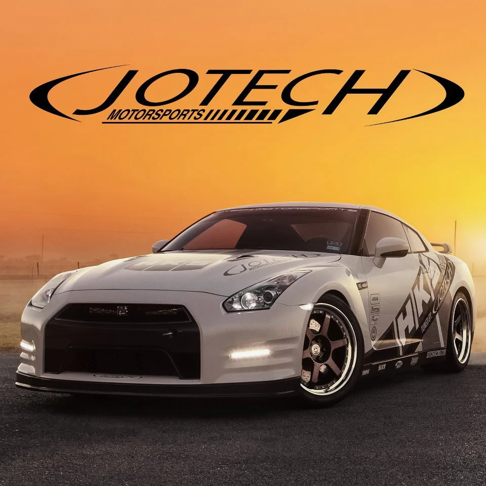 A white Nissan GT-R with Jotech Motorsports livery and aftermarket wheels, parked at sunset with the Jotech logo overhead.
