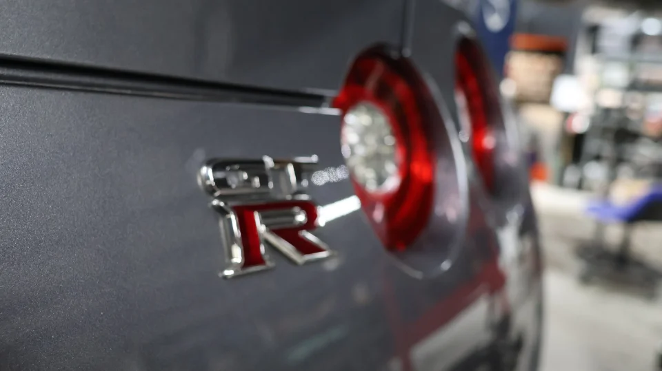 A close-up detail shot of the rear of a grey Nissan GT-R, showing the GT-R badge and circular taillights.