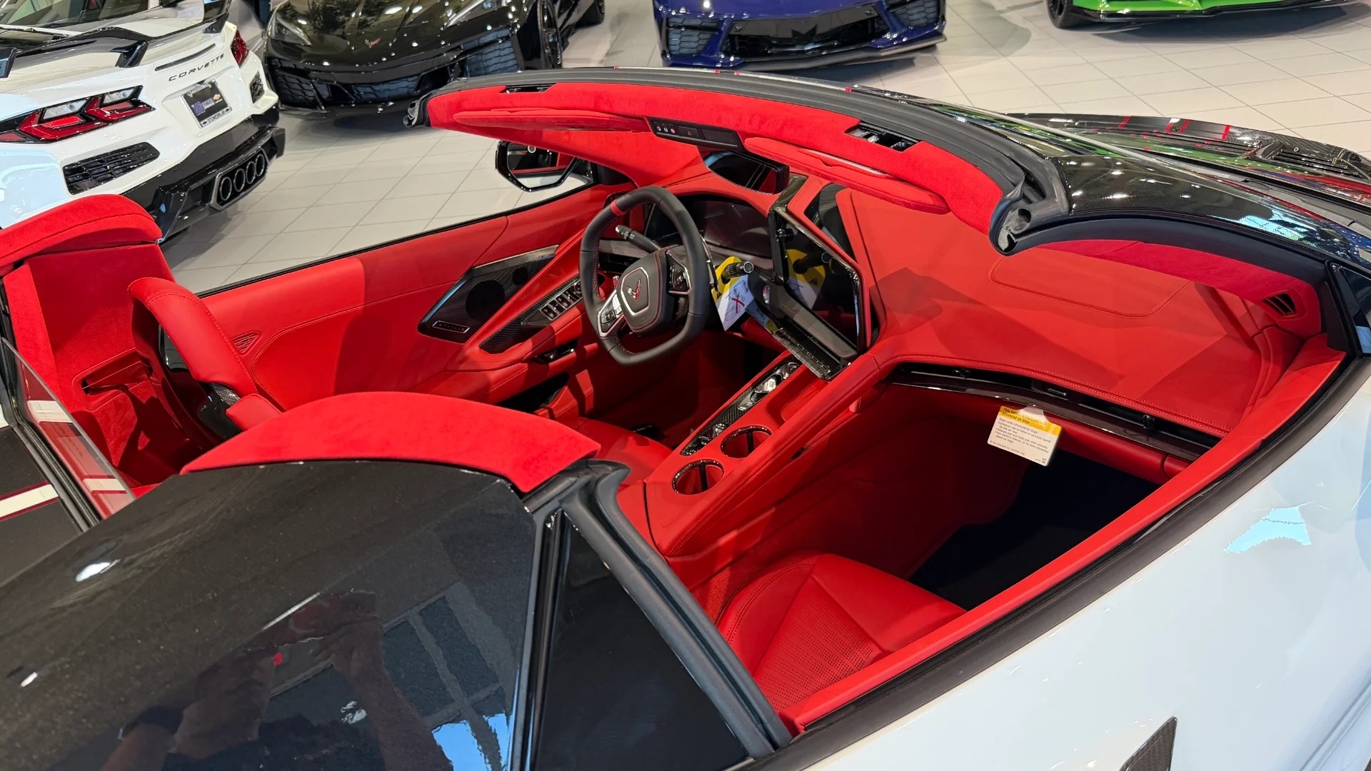 A white Chevrolet Corvette C8 convertible with a striking red interior, parked in a showroom.