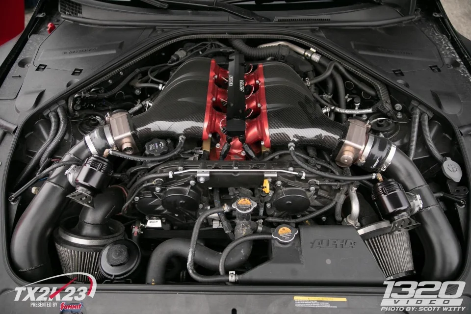 Close-up of a highly modified Nissan GT-R R35 engine bay featuring Alpha Performance carbon fiber intake manifolds.