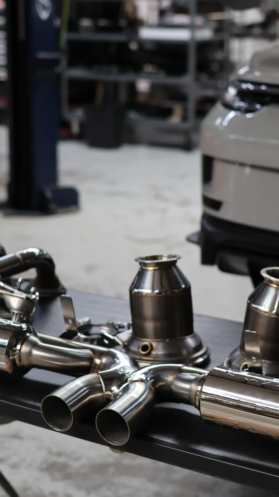 Polished stainless steel exhaust system components, including downpipes and catalytic converters, laid out on a table in a performance tuning shop.