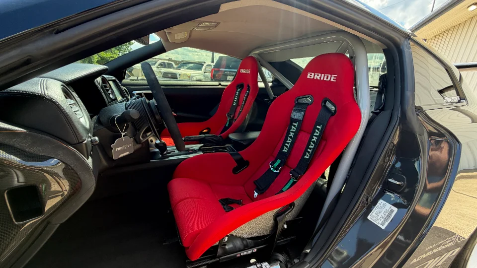 Interior view of a Nissan GT-R featuring red Bride racing seats with Takata harnesses and a roll cage.