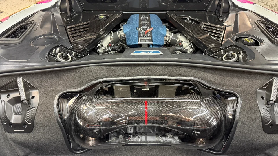 A detailed view of a modified Corvette C8 engine bay featuring a blue supercharger cover and carbon fiber intake system.