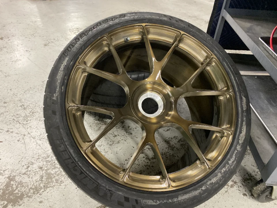 Bronze multi-spoke wheel with a Michelin Pilot Sport Cup 2 tire on a shop floor