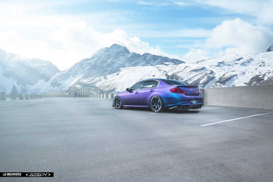A purple and blue chameleon-wrapped Infiniti G37 sedan with aftermarket wheels parked in a mountain parking lot.