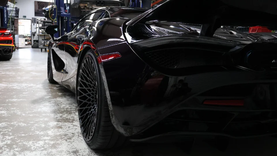 A black McLaren 720S with custom wheels parked inside a performance tuning shop.