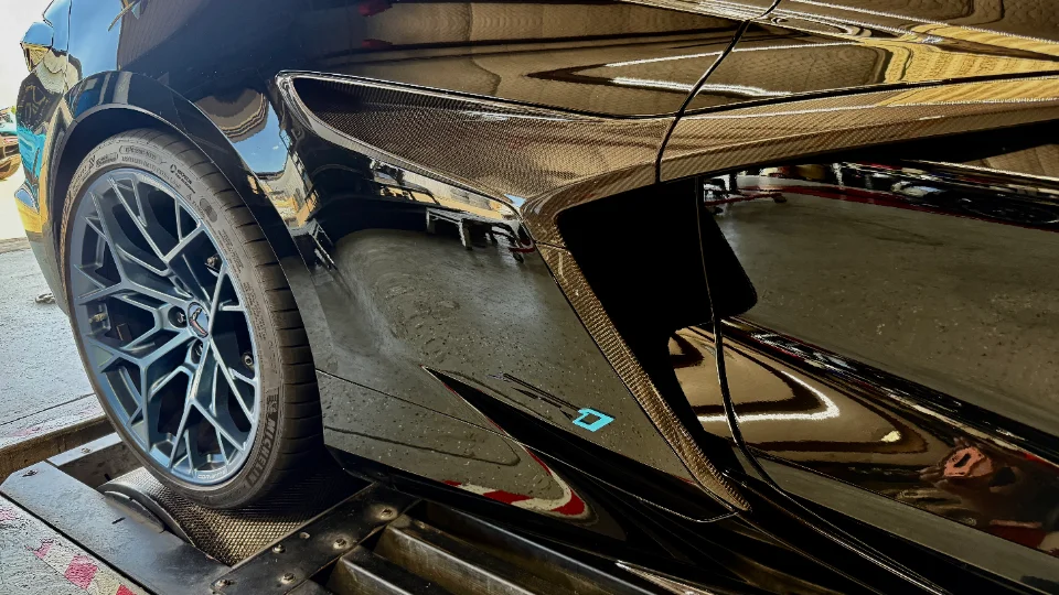 Close-up of a black C8 Corvette on a dyno, showcasing the wheel, tire, and carbon fiber side intake.