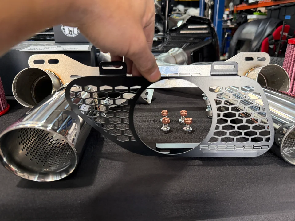 Close-up of Fabspeed exhaust components, including polished tips and a honeycomb heat shield, displayed in a shop.