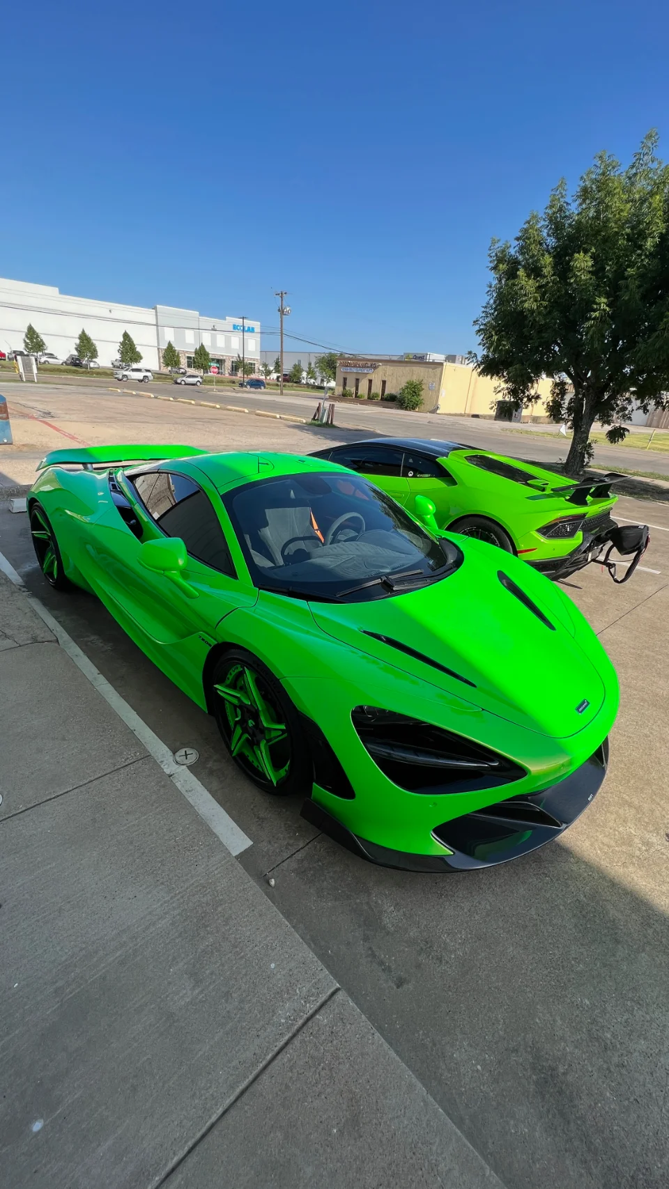 Two vibrant green supercars, a McLaren and a Lamborghini, parked side-by-side in a sunny outdoor setting.