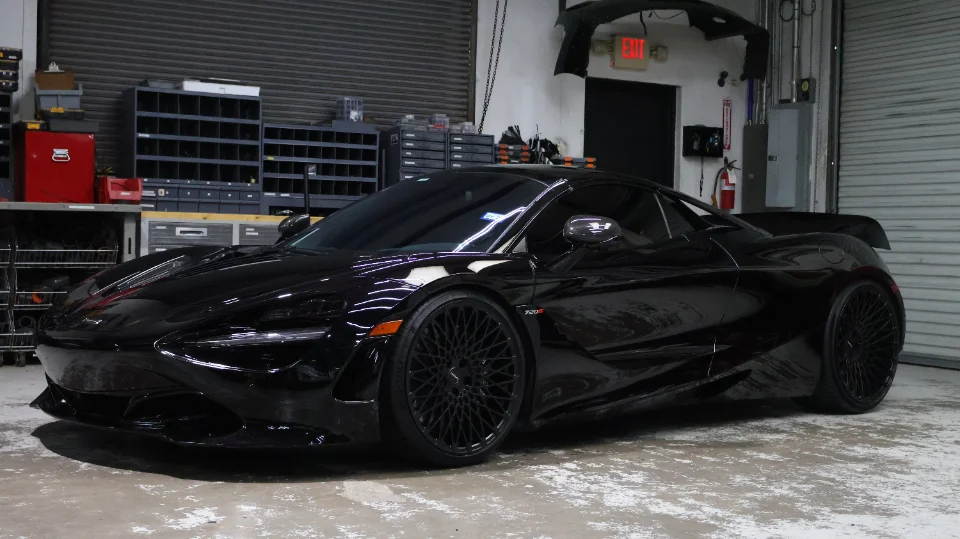 A black McLaren 720S with custom black wheels parked inside a performance tuning shop.