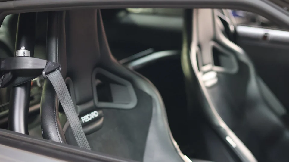 Close-up interior view of a performance car showing Recaro racing seats, a roll cage, and safety harnesses.