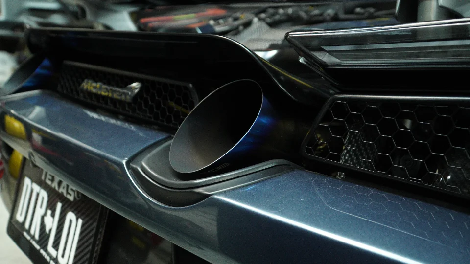 A close-up detail shot of a McLaren's blue-tinted titanium exhaust tip and rear bumper.