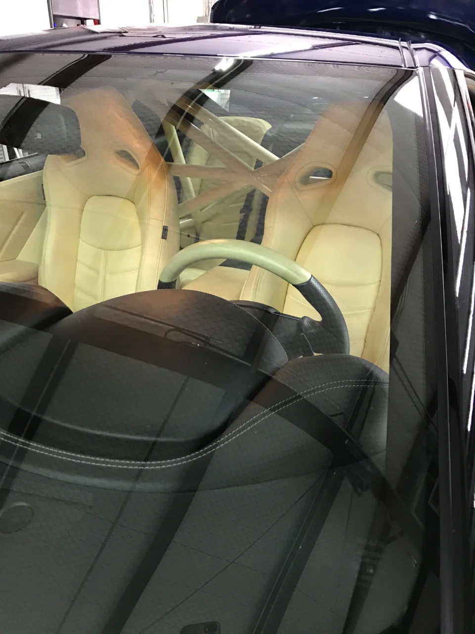 Interior view of a performance car showing beige racing seats, a roll cage, and steering wheel.