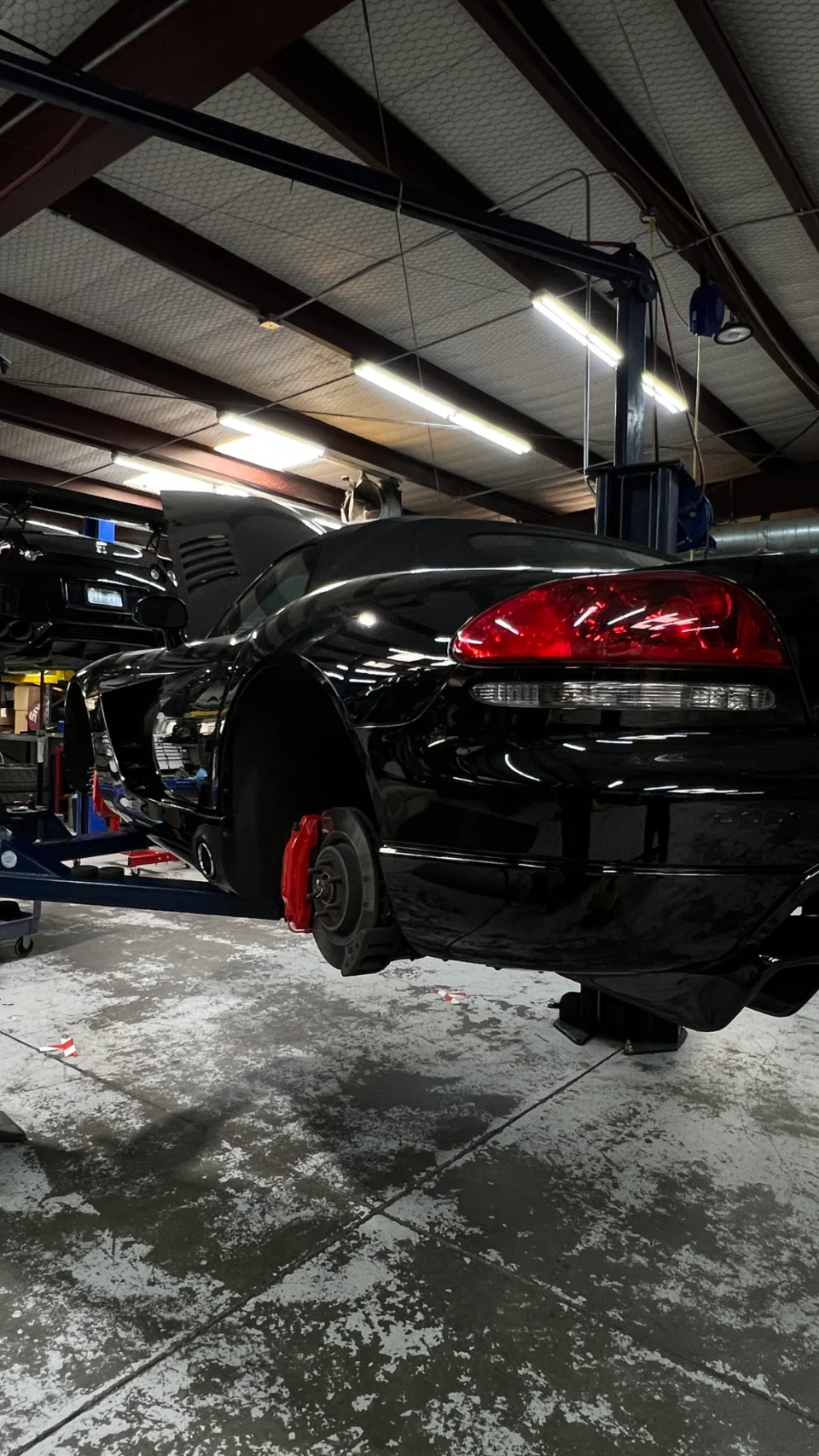 A black Dodge Viper on a lift in a performance shop, with its wheels removed, showcasing red brake calipers.