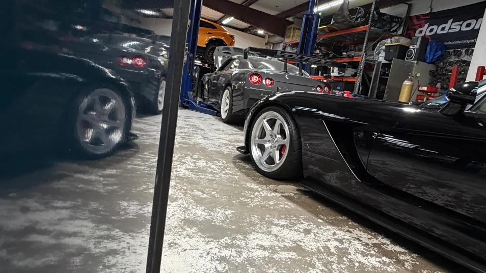 High-performance cars including a black Dodge Viper and a grey Nissan GT-R on a lift inside a Jotech Motorsports tuning shop.