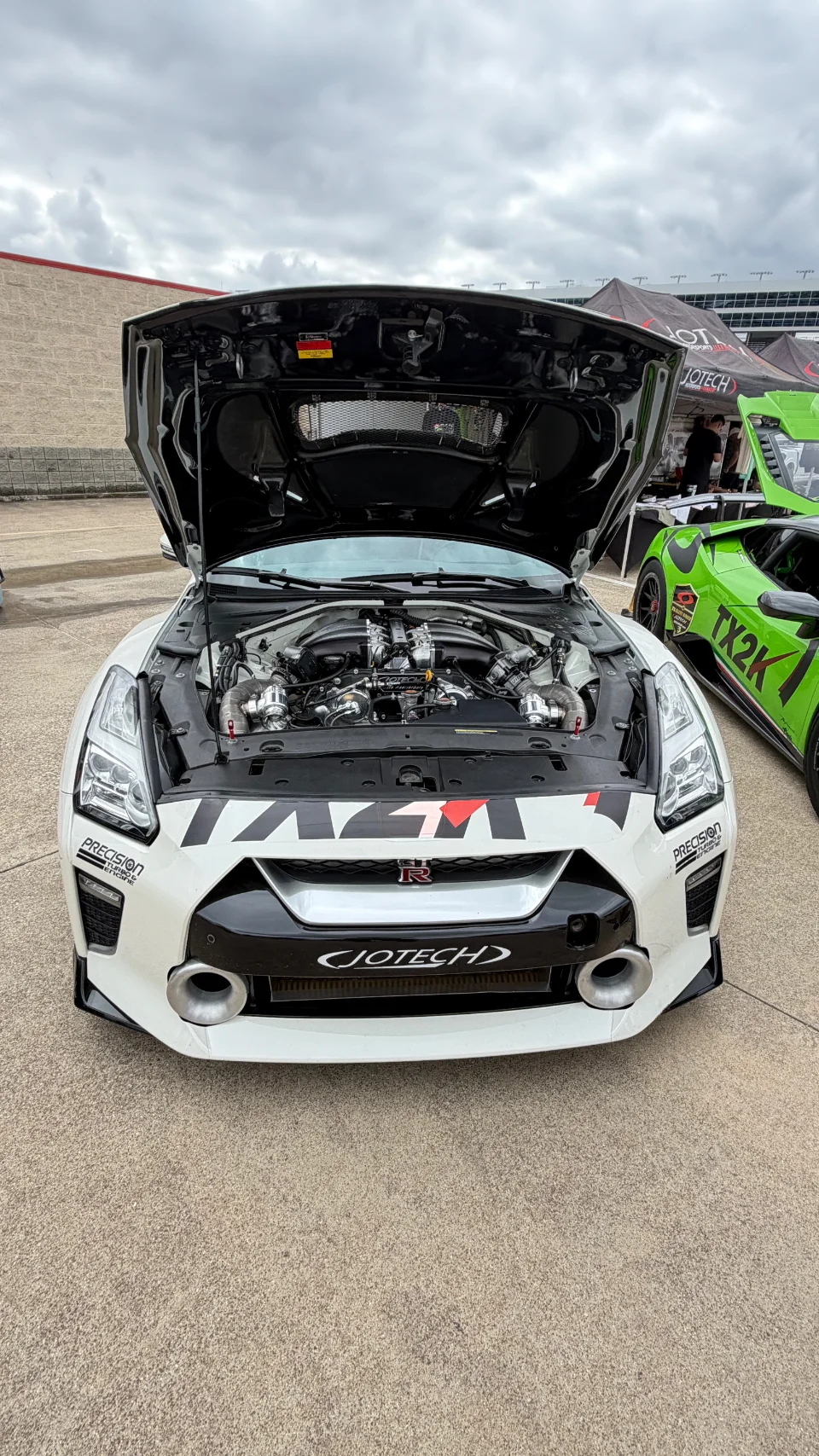 A white Nissan GT-R with its hood open, showcasing a highly modified twin-turbo engine by Jotech Motorsports.