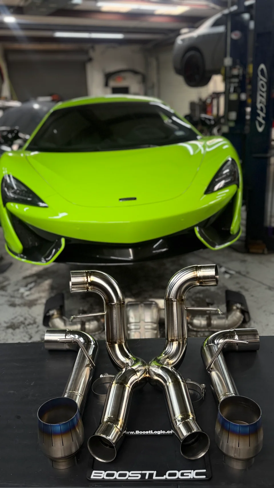 A lime green McLaren supercar in a performance shop with a Boost Logic aftermarket exhaust system laid out in the foreground.