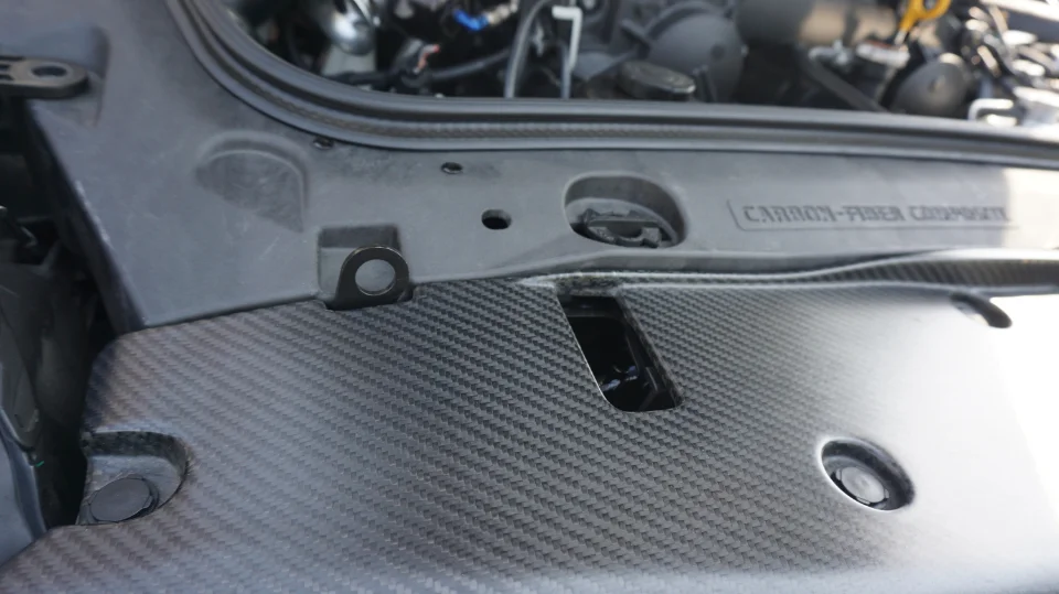 Close-up of a carbon fiber composite engine bay cover on a performance car, highlighting the weave pattern.