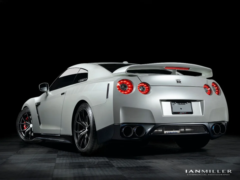 A white Nissan GT-R R35 with aftermarket wheels and exhaust, professionally photographed in a studio setting.