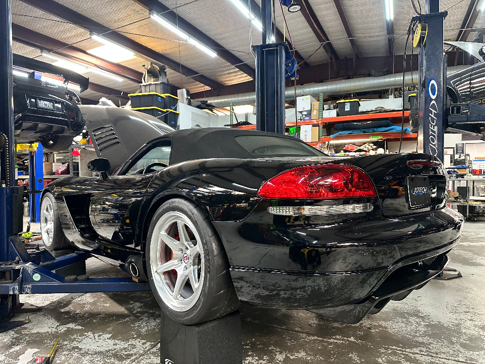A black Dodge Viper convertible on a lift in a performance tuning shop, showcasing aftermarket wheels and red brake calipers.