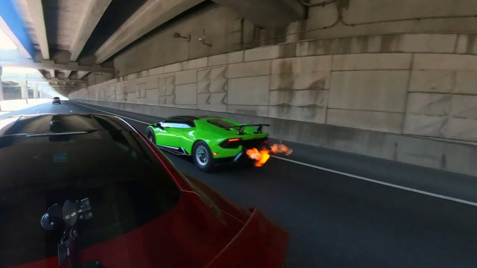 A vibrant green Lamborghini Huracan with a large rear wing, shooting flames from its exhaust while driving under a highway overpass.