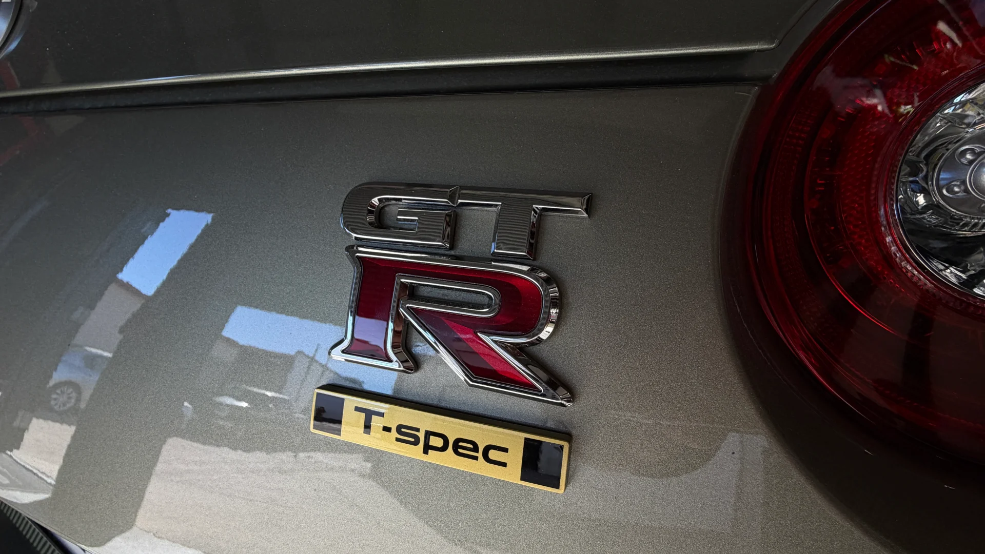 Close-up of a Nissan GT-R T-spec badge and taillight on the rear of the car, showcasing the vehicle's model and trim.