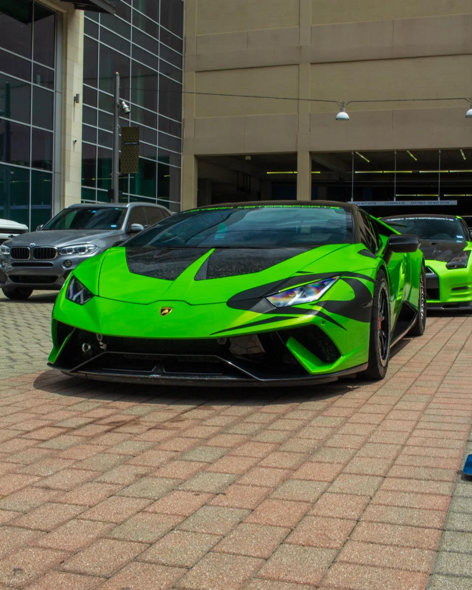 Bright green Lamborghini Huracan with black accents and a Nissan GT-R parked on a brick sidewalk outside a building.