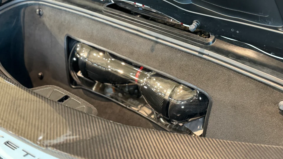 A close-up view of a carbon fiber intake system installed in the engine bay of a Corvette C8.