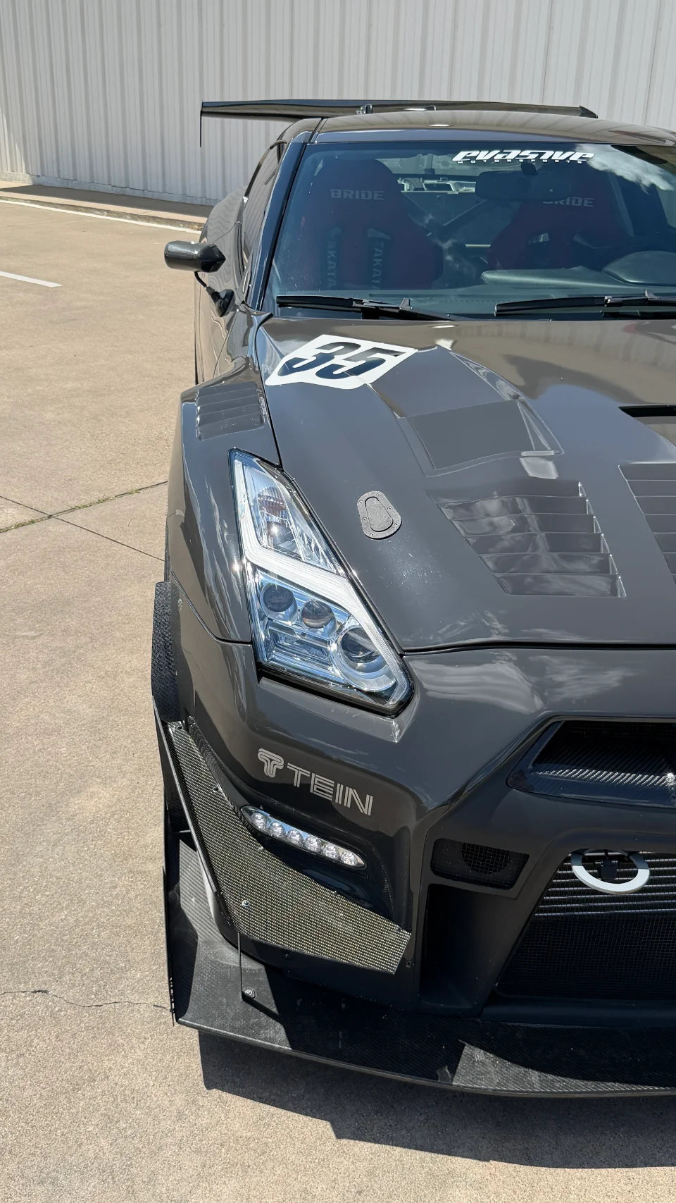 Close-up of a modified gray Nissan GT-R R35 featuring a widebody kit, carbon fiber aero, and a vented hood.