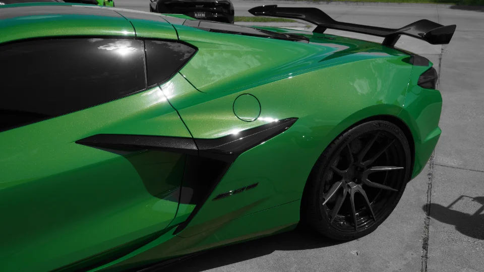 A vibrant green C8 Corvette with custom black wheels and a large rear wing, captured from a rear quarter angle.
