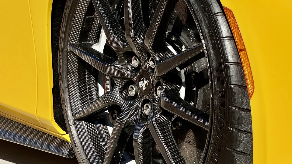 A close-up detail shot of a yellow Ferrari's carbon fiber wheel with Michelin tire and visible brake caliper.