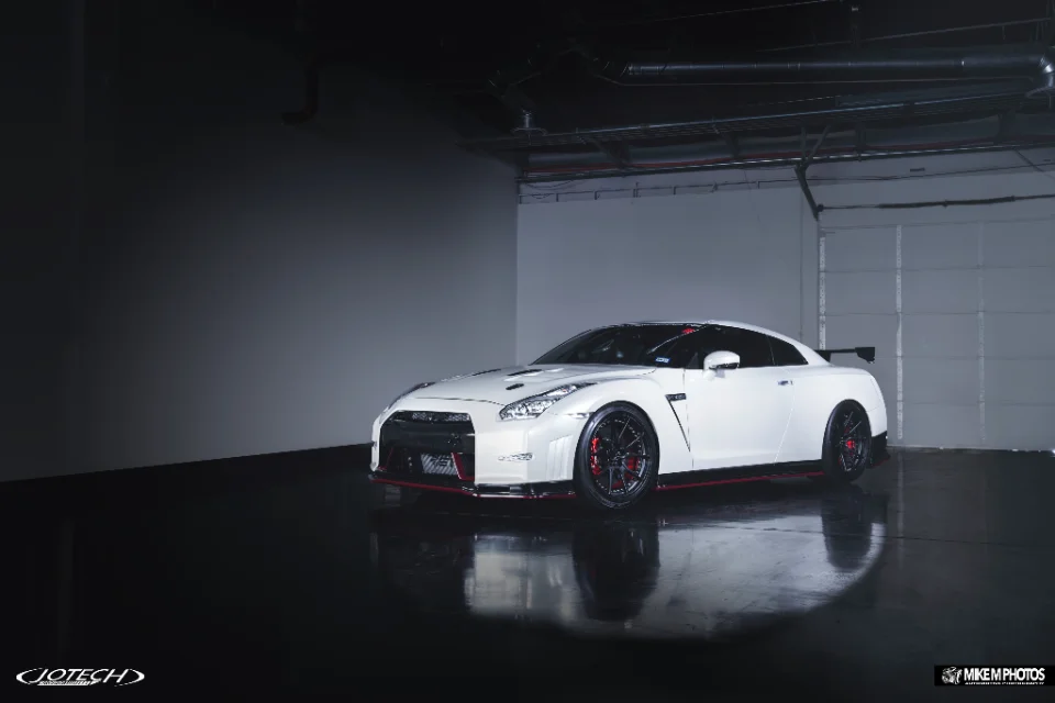 A white Nissan GT-R with aftermarket wheels and aero modifications parked in a professional studio setting.