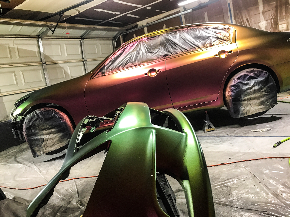 Infiniti G37 sedan undergoing a chameleon paint job in a garage, with the front bumper detached and covered for painting.