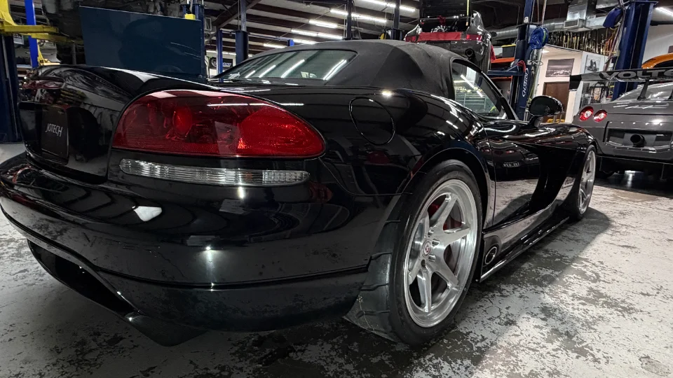 Rear three-quarter view of a black Dodge Viper convertible with aftermarket wheels and performance tires in a Jotech Motorsports shop.