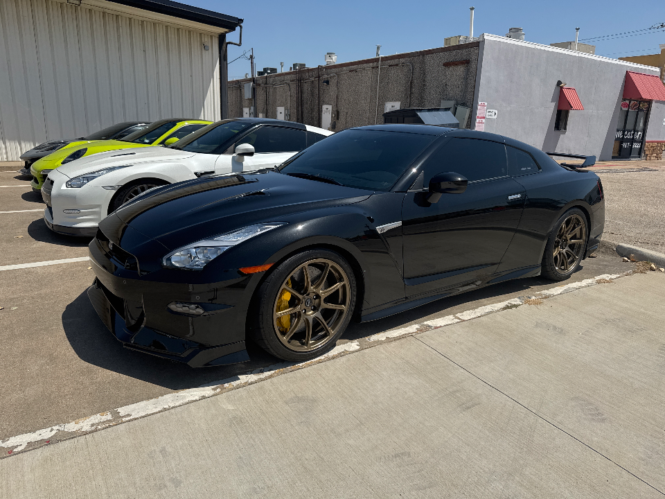 A line of high-performance cars, including black, white, and neon green Nissan GT-Rs and a McLaren, parked outside.