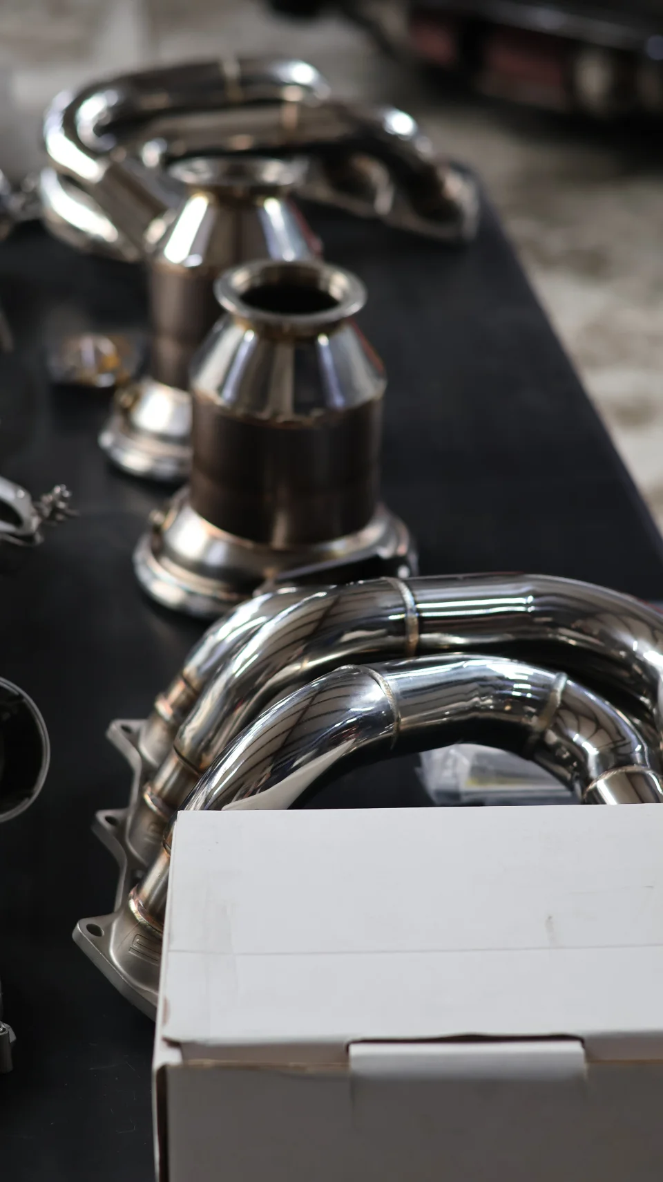 Close-up of shiny stainless steel performance exhaust components, including downpipes and catalytic converters, displayed on a table.