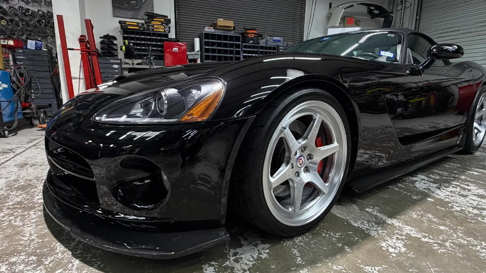 A black Dodge Viper with custom silver wheels and a carbon fiber front splitter parked inside a performance tuning shop.