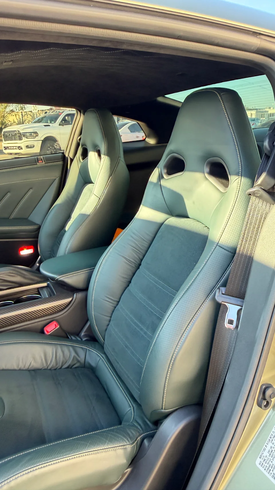 Interior view of a Nissan GT-R featuring dark leather and suede sport seats with white stitching and carbon fiber trim.